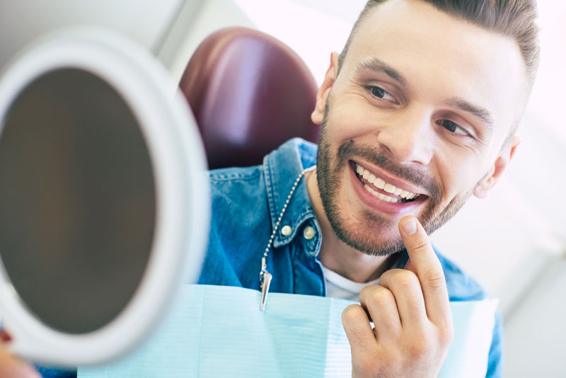 a dental patient in a patient chair smiling into a mirror because he has been treated with cosmetic dentistry.