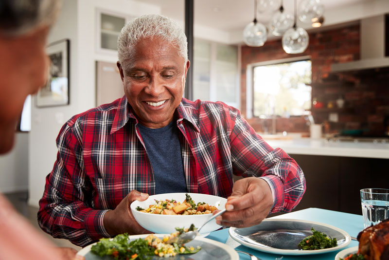 a dental implant patient smiling over his meal at the dinner table because he was treated with guided dental implant surgery.