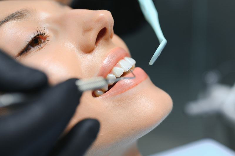 Doctor examining patient's teeth, closeup. Black gloves with dental tool in hand, up-close image of dental examination