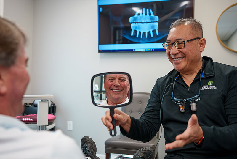 Doctor holding up mirror so patient can see his brand new smile